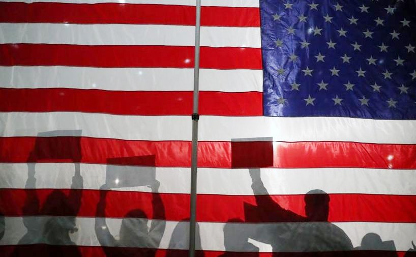 Silhouettes of attendees holding signs in front of an American flag